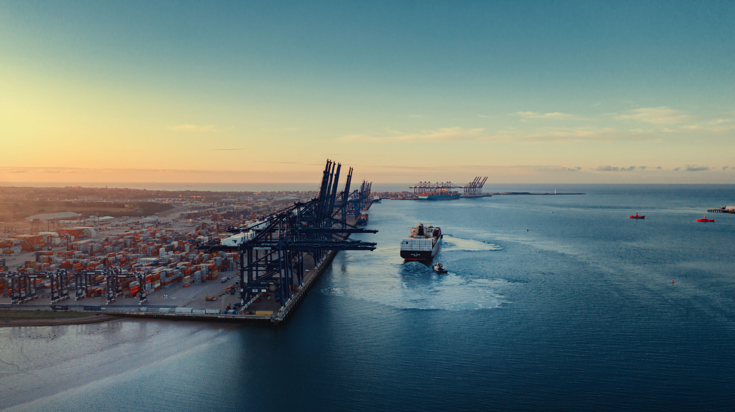 Sunrise over Felixstowe Container Port as two tugs shepherd a container ship away from the harbour wall stock photo