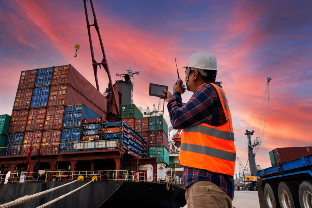 Yard Operator talking on radio and using tablet while container ship is being loaded